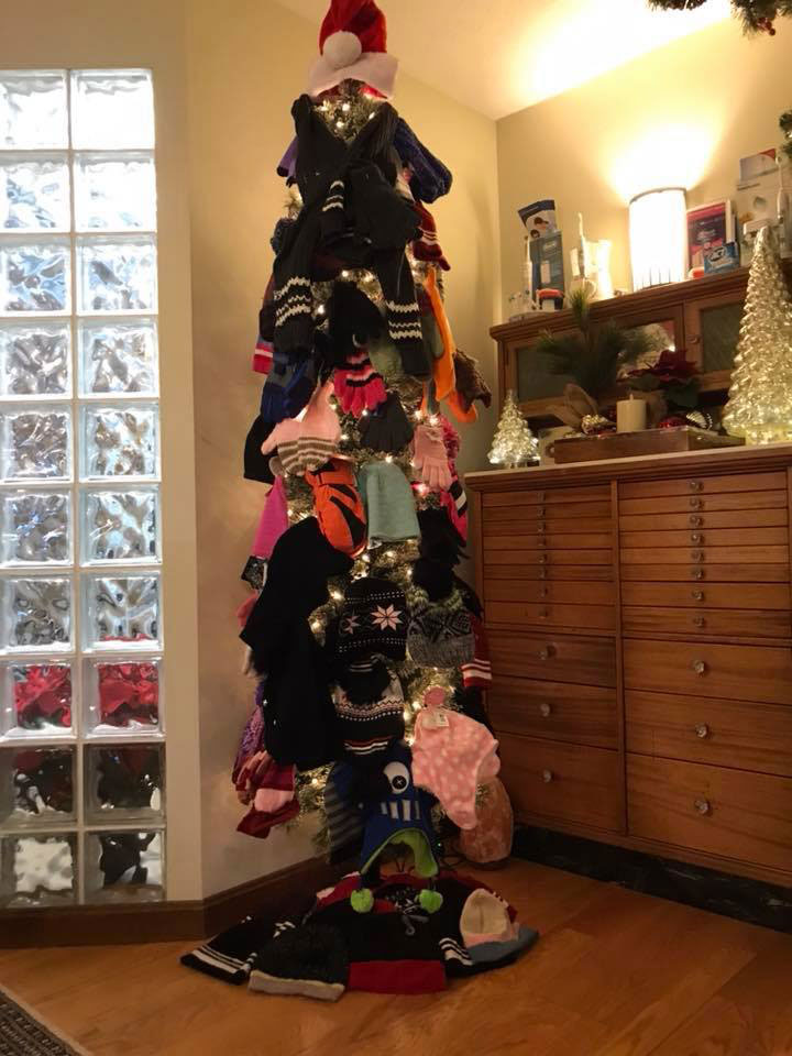 This is a photograph of a Christmas tree decorated with various items, including clothes, toys, and festive decorations, placed indoors during the holiday season.