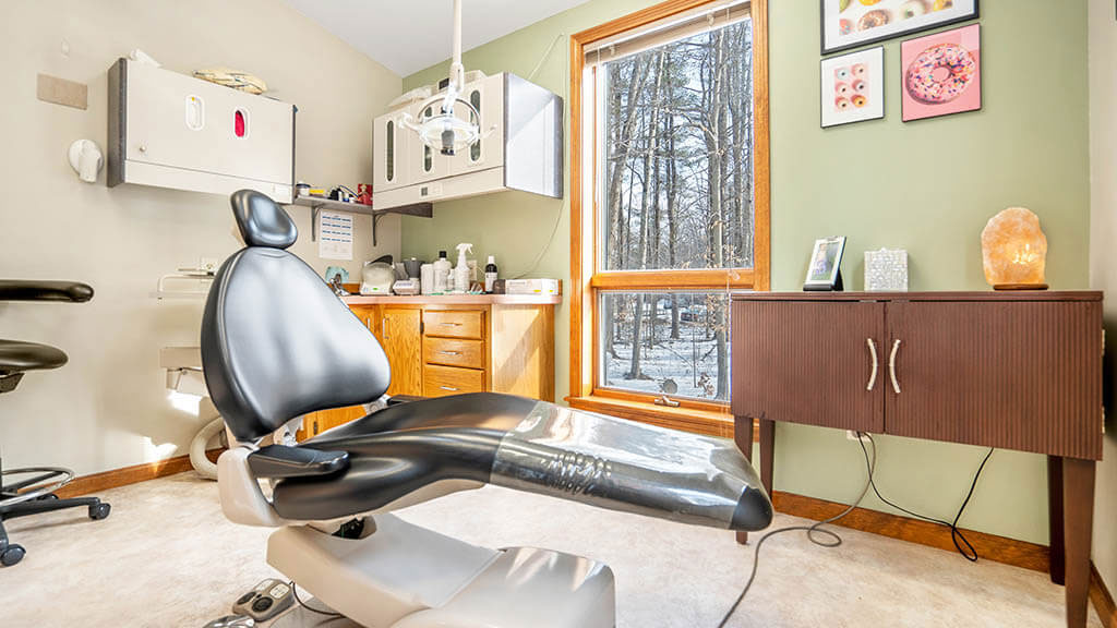 Dental office interior with dental chair, counter, and various equipment in the background.