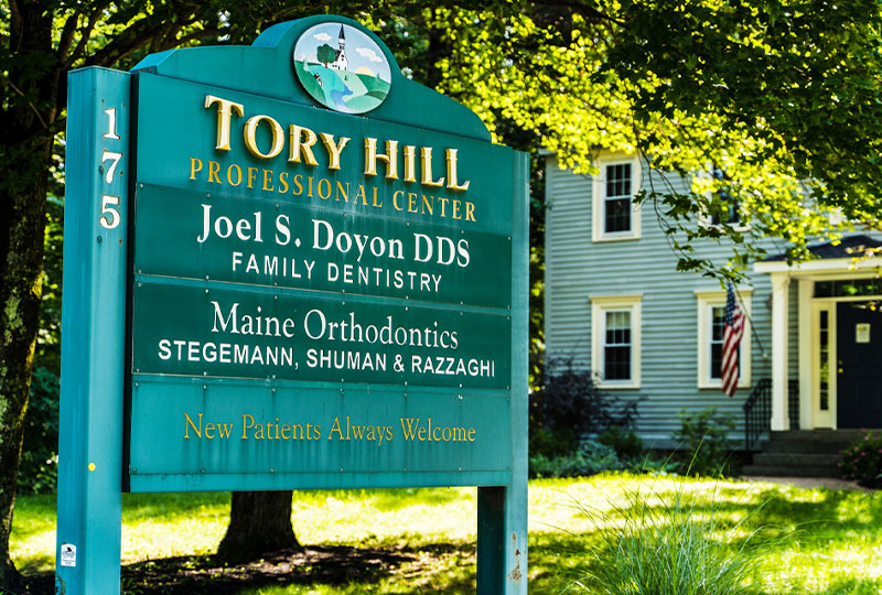 The image shows a sign indicating  Twin Hill Professional Center  with names listed below, located near a building with a tree in front and a clear sky above.