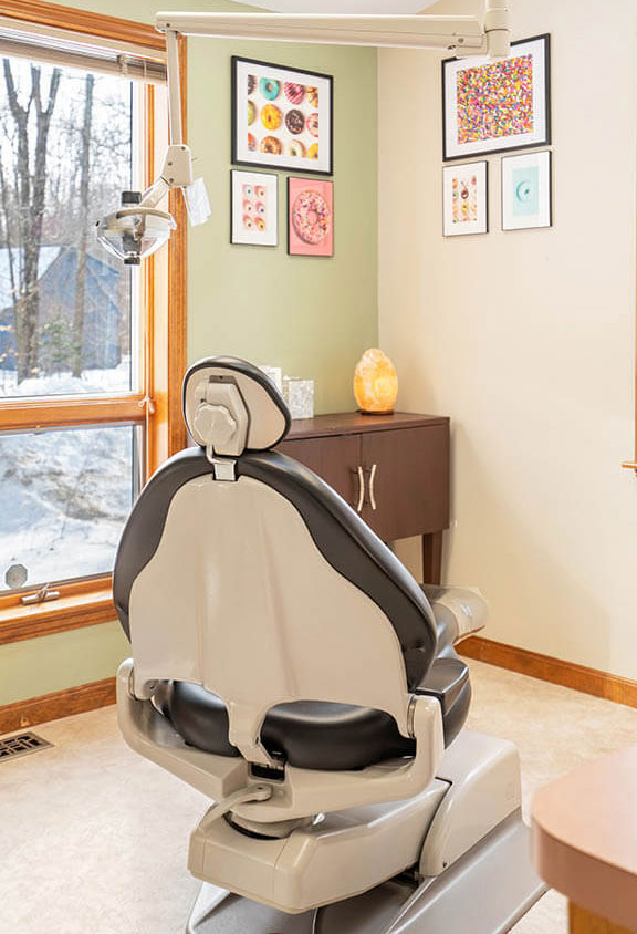The image shows a dental office setting with a modern dental chair and a window view.