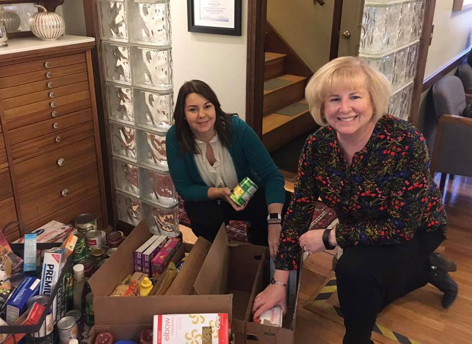 Two women standing next to boxes filled with food items, likely preparing for a donation or distribution event.
