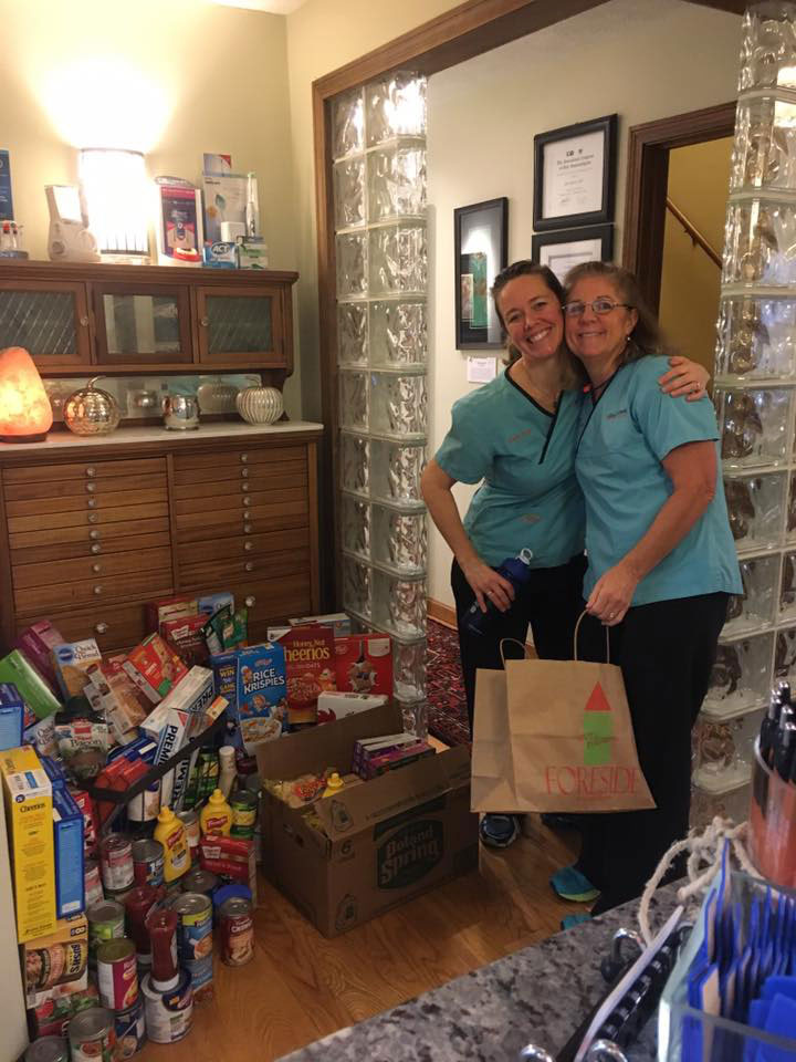 Two women standing together in front of a table filled with various food items, smiling at the camera.