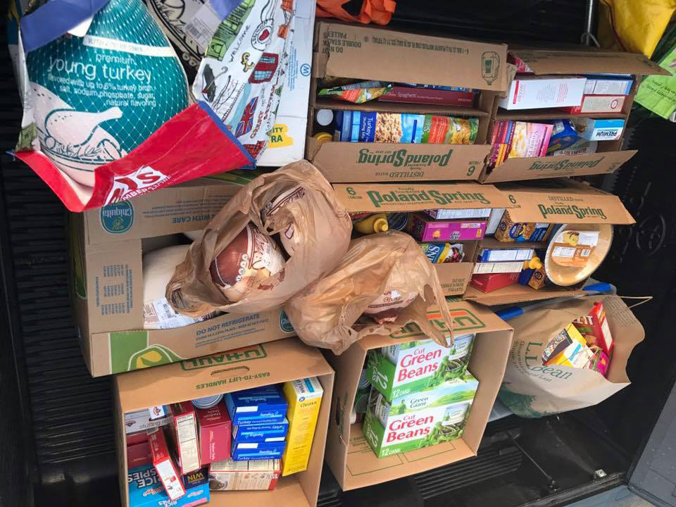The image shows a collection of food items, including cereal boxes and possibly other packaged goods, displayed on an outdoor surface with a cardboard box at the center, suggesting a makeshift marketplace or donation drive.