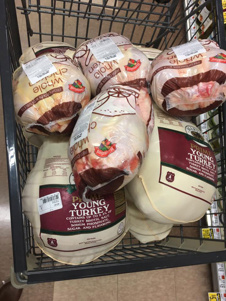 The image shows a shopping cart filled with raw poultry, including turkeys and chickens, displayed for sale at a grocery store.
