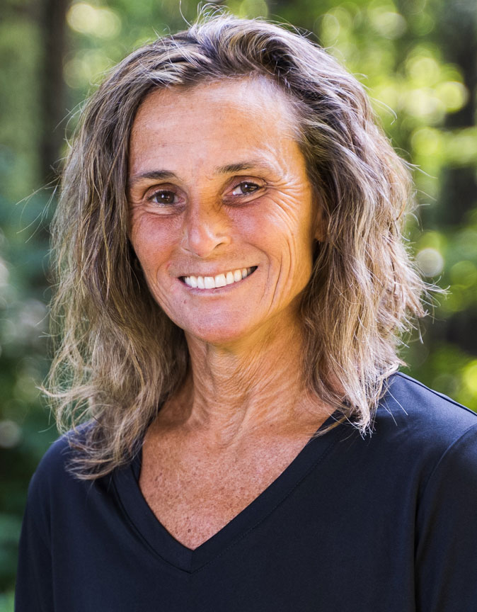 The image shows a woman with shoulder-length hair, wearing a black top, smiling at the camera.