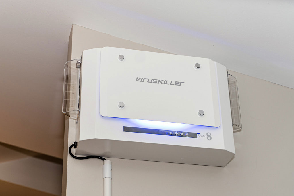 The image shows a white device with a blue light attached to a wall, labeled 'virus killer,' indicating its purpose for cleaning air from viruses.