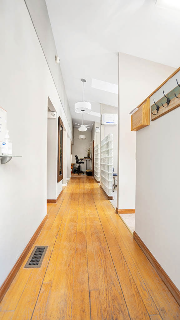 The image shows a long hallway with wooden flooring, leading to an open door at the end.