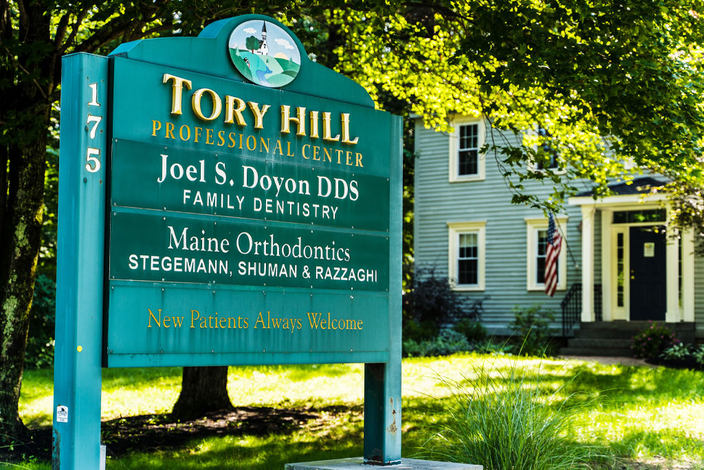 The image shows a sign for 'Troy Hill Professional Dental Center' with the names of dental professionals listed below, set against a background of a building and trees, indicating an outdoor location.