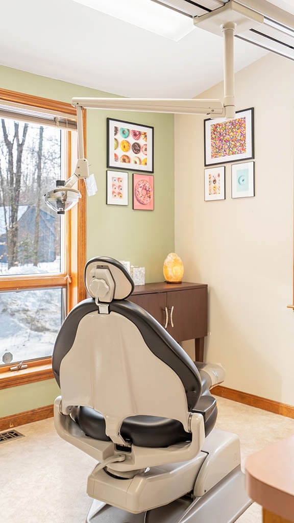 The image depicts a well-equipped dental office with a modern dental chair, a large mirror, and various pieces of dental equipment visible.