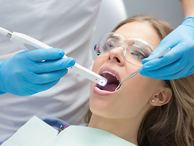 A woman receiving dental care with a dental device inserted into her mouth, being held by a dental professional wearing blue gloves and a protective face mask.